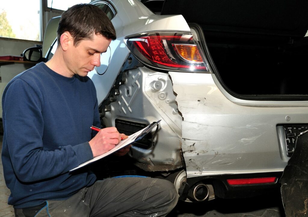 Persona al lado de coche accidentado rellenando los papeles del seguro para calcular indeminzación por accidente de tráfico